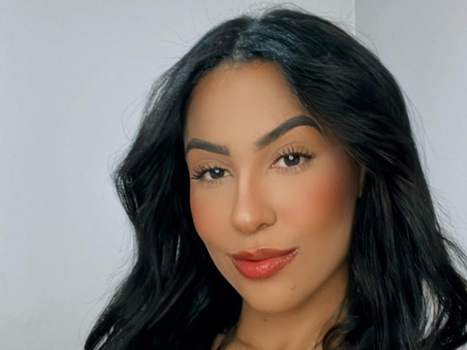 EllenS69 has black wavy hair, thick eyebrows, red lipstick, and a subtle smile. Her brown skin has a smooth, even tone. She looks attractive and confident.