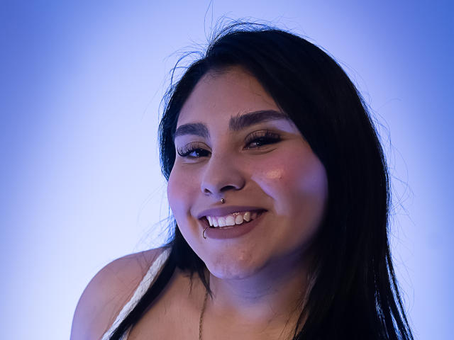 KatiaRodriguez has dark, straight hair, a nose ring, and a lip piercing. She's smiling with visible drool and a slightly flushed face, wearing a white top.