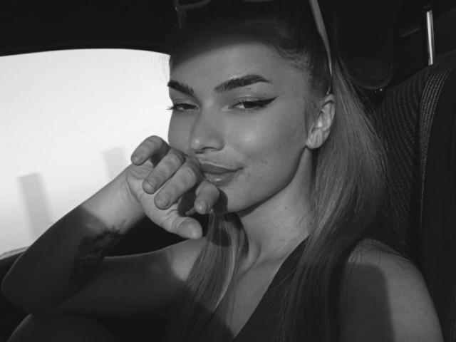 IngridI has a cute, smirking face, long ponytail, and sharp winged eyeliner. She's resting her hand near her mouth, showing a subtle smile, in a black-and-white shot.