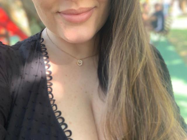 Erinn99-hot has light skin, subtle freckles, and a small necklace with a heart charm. She's wearing a black, crotched top, showing some cleavage and a gentle smile.