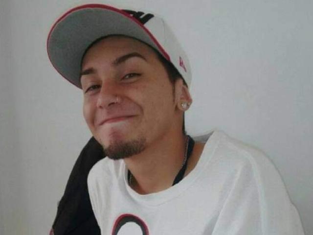 JohnDupontt, a dude with light skin, a small nose ring, and a goatee, wearing a white cap and shirt, smiling slightly. He's got small earrings and a casual look.