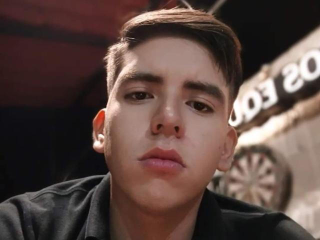 AnteRona has a pensive expression with slightly parted lips, short brown hair, and a black shirt. His face is centered, and the lighting highlights his youthful, pale skin.