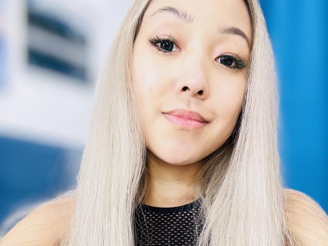 RenyLime a de longs cheveux blonds et lisses, des yeux verts avec de longs cils noirs, des lèvres roses et un teint clair. Elle porte un haut en maille noire et a l'air adorable..
