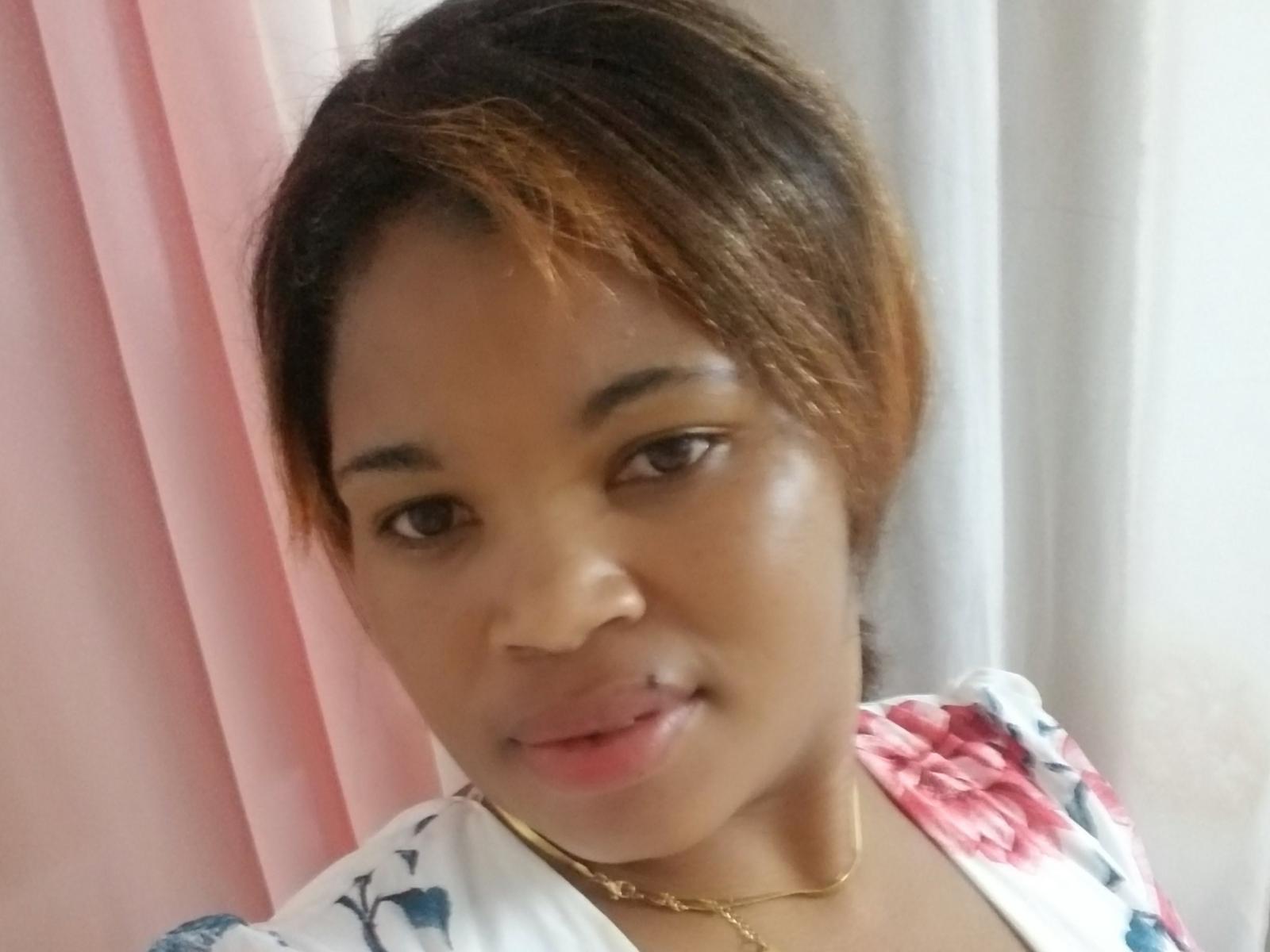 Sourayah69 with brown eyes, light brown skin, and short brown hair with highlights, wearing a floral top, and a gold necklace, smiling slightly.