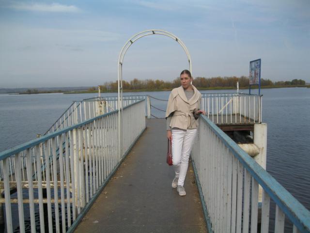 LoveFM-hot with short brown hair, wearing a beige jacket, white pants, and white shoes, walks on a blue and white metal bridge holding a red bag.