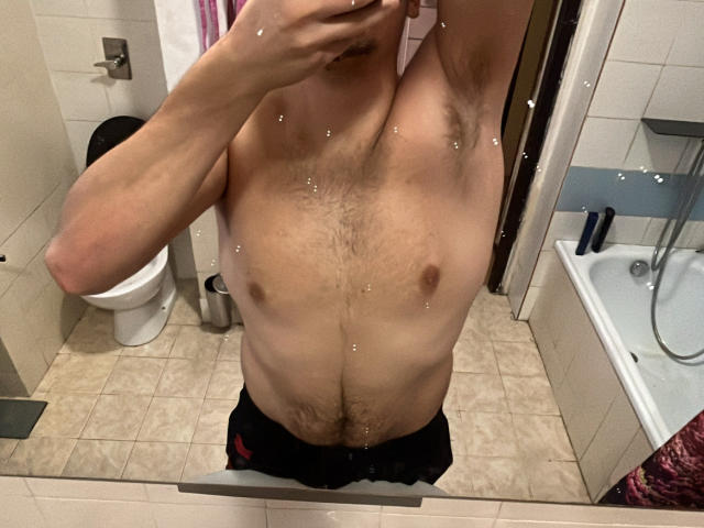 MarkXHot's bare chest with small, dark nipples and a hairy, muscular upper body in a mirror selfie. Visible armpit hair, mirror reflection, and bathroom setting.