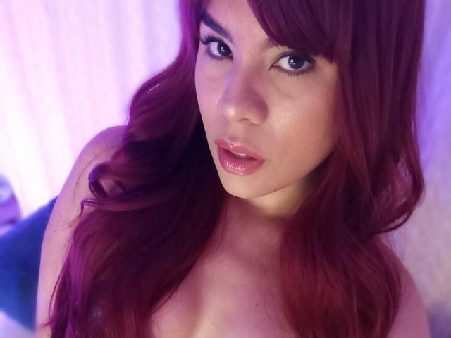 LilsWay has shiny pink lips, long red hair, and a slightly parted mouth. Her bare shoulders are visible, and she's looking at the camera with a sultry expression.