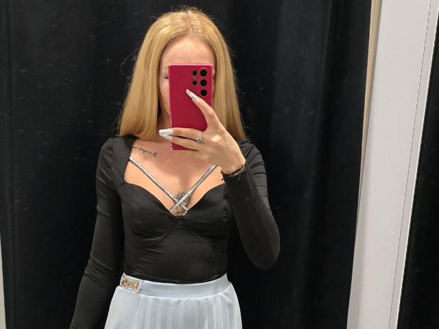 LoreenBlanc met lang blond haar, een zwarte top met lange mouwen, een witte rok, die een rode telefoon vasthoudt, met kleine borsten, op een zwarte achtergrond, een spiegelzelfportret..