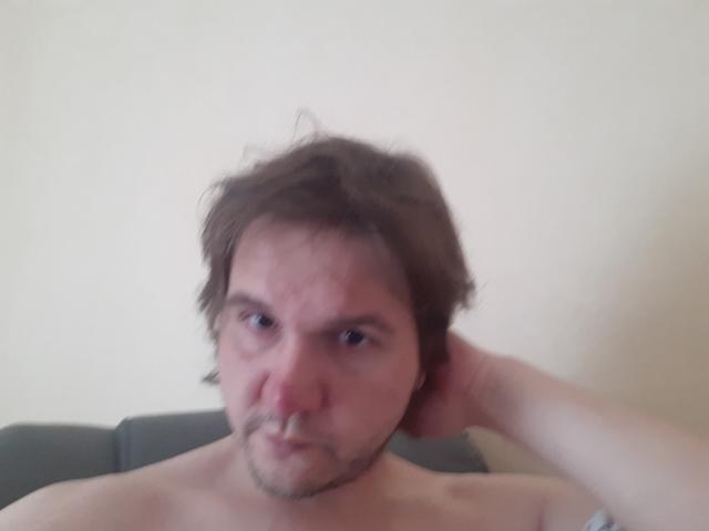NectarineFad has a blurry, slightly annoyed face with messy brown hair, a light beard, and his hand behind his head, shirtless, against a plain background.