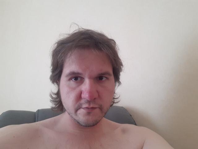 NectarineFad has a chubby face, messy brown hair, and a light beard, looking directly at the camera with a neutral expression, shirtless, against a plain background.