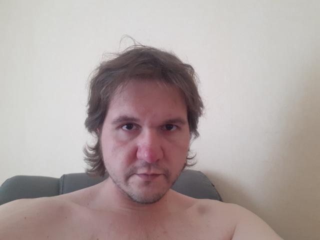 NectarineFad has a slightly puffy nose, messy brown hair, and a serious expression. He's shirtless with a gray headrest behind him. His chest is visible.