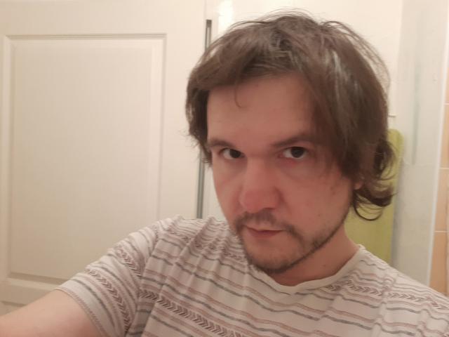 NectarineFad has messy brown hair, a light beard, and is wearing a striped shirt. He's staring intensely with a slight smirk. His nose is a bit red.
