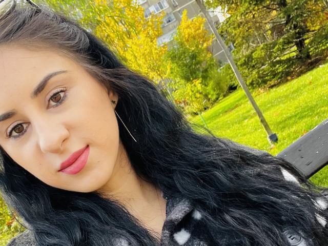 De selfie van IreneSkye toont haar met lang, zwart, golvend haar, bruine ogen, roze lippen en een lichte huid. Ze draagt een zwart-wit gestreept top, met groen gras op de achtergrond..