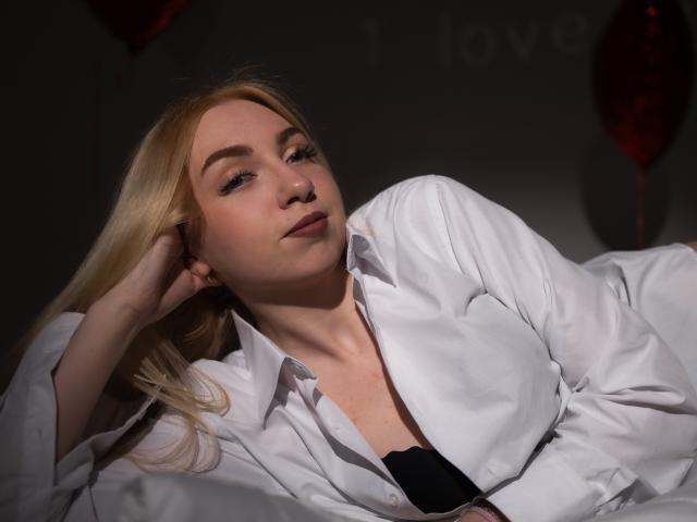 Beatrice: Blondhaarige Frau, die ein weißes Hemd mit offenem Kragen trägt, ein schwarzes BH ist sichtbar, liegt, Hand in der Nähe des Kopfes, weiches Licht, leichtes Lächeln, entspannt, rote Ballons im Hintergrund..