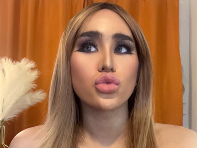 Alexaonfire69x has pouty pink lips, heavy black eyeliner, long blonde hair, and is pouting at the camera with a cute expression, her tits barely visible.