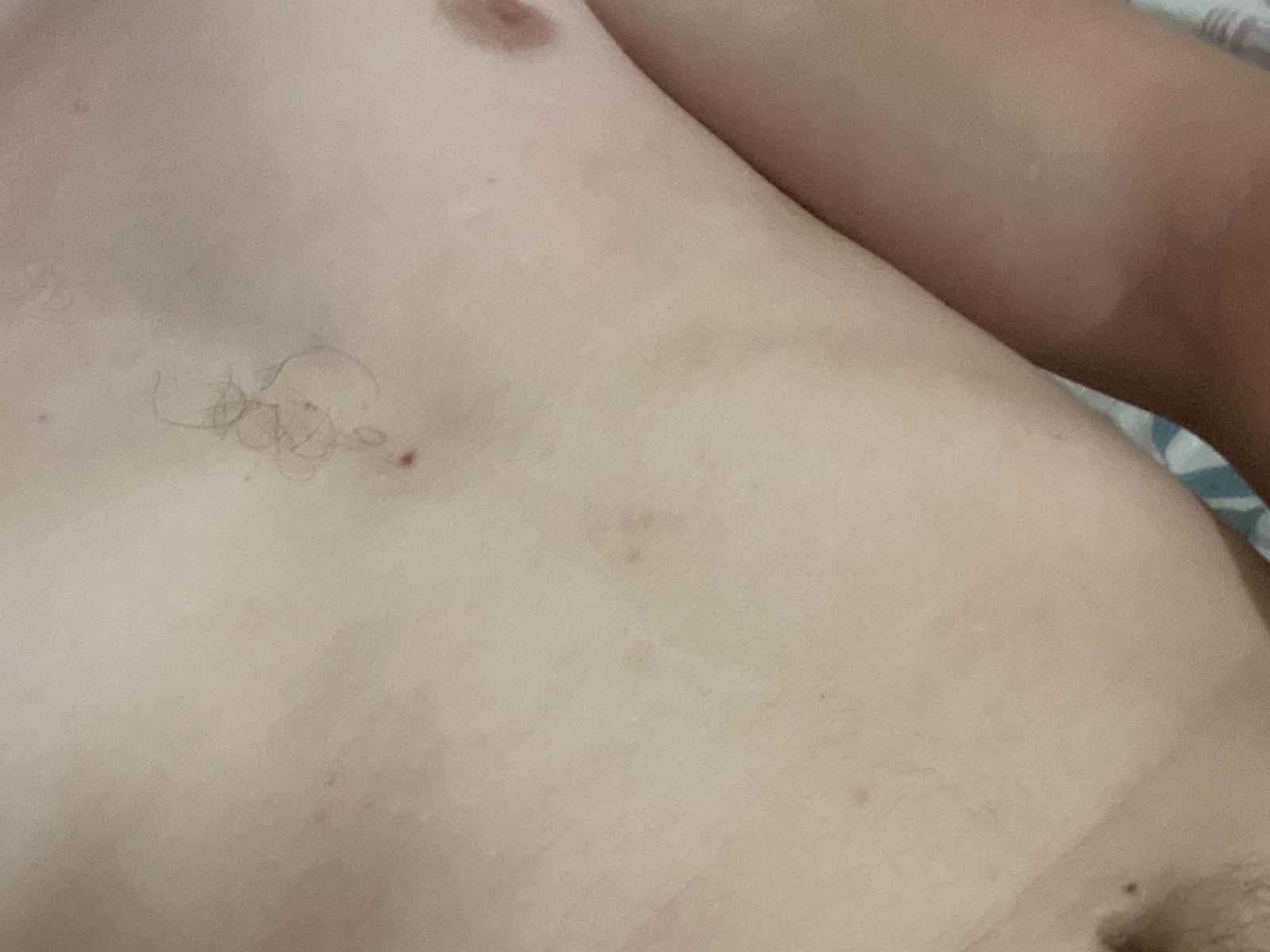 Chaux69's bare, light-skinned torso with small nipples, subtle tan lines, and a faint, tiny tattoo of a simple line drawing near the left side of their ribcage.