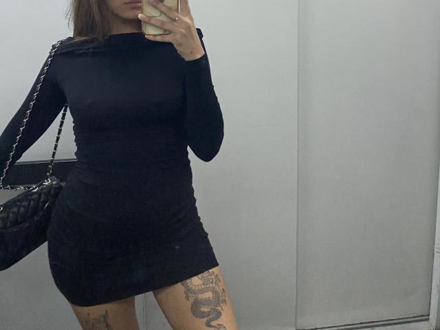 Kametia indossa un abito nero aderente, a maniche lunghe, tiene in mano il telefono, è un selfie allo specchio, porta una borsa nera con una catena, ha un tatuaggio visibile sulla coscia destra, ha i capelli castani, il viso non è visibile..