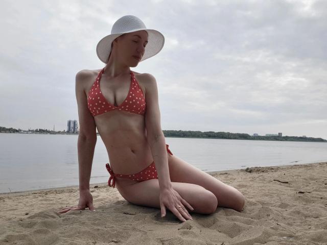 LoveFM-hot with pale skin, small tits, and a red polka-dot bikini, wearing a white sun hat, sitting on sandy beach, knees bent, arms resting, overcast sky.