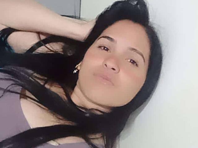 MartinaDupont with black hair, brown eyes, and a slight pout, wearing a purple top, hand in hair, looking at camera, soft light, slight blush on cheeks.