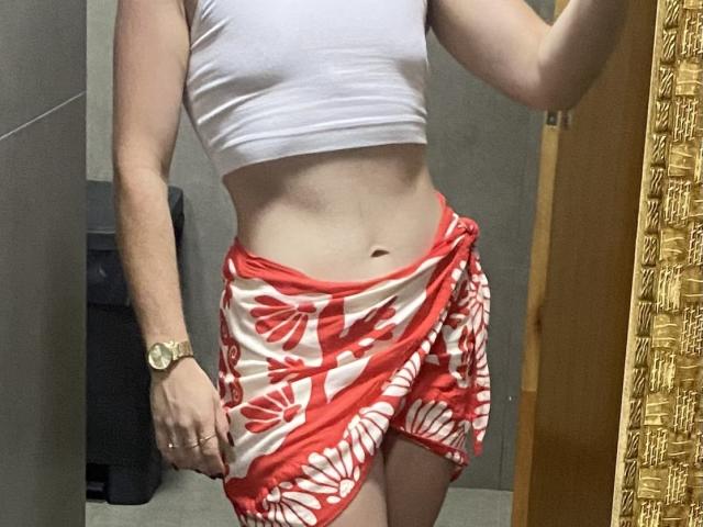 DrikaHottie wearing a white crop top, red and white floral sarong, gold watch, standing with visible abs, no pants, her tits are small, her ass is covered.