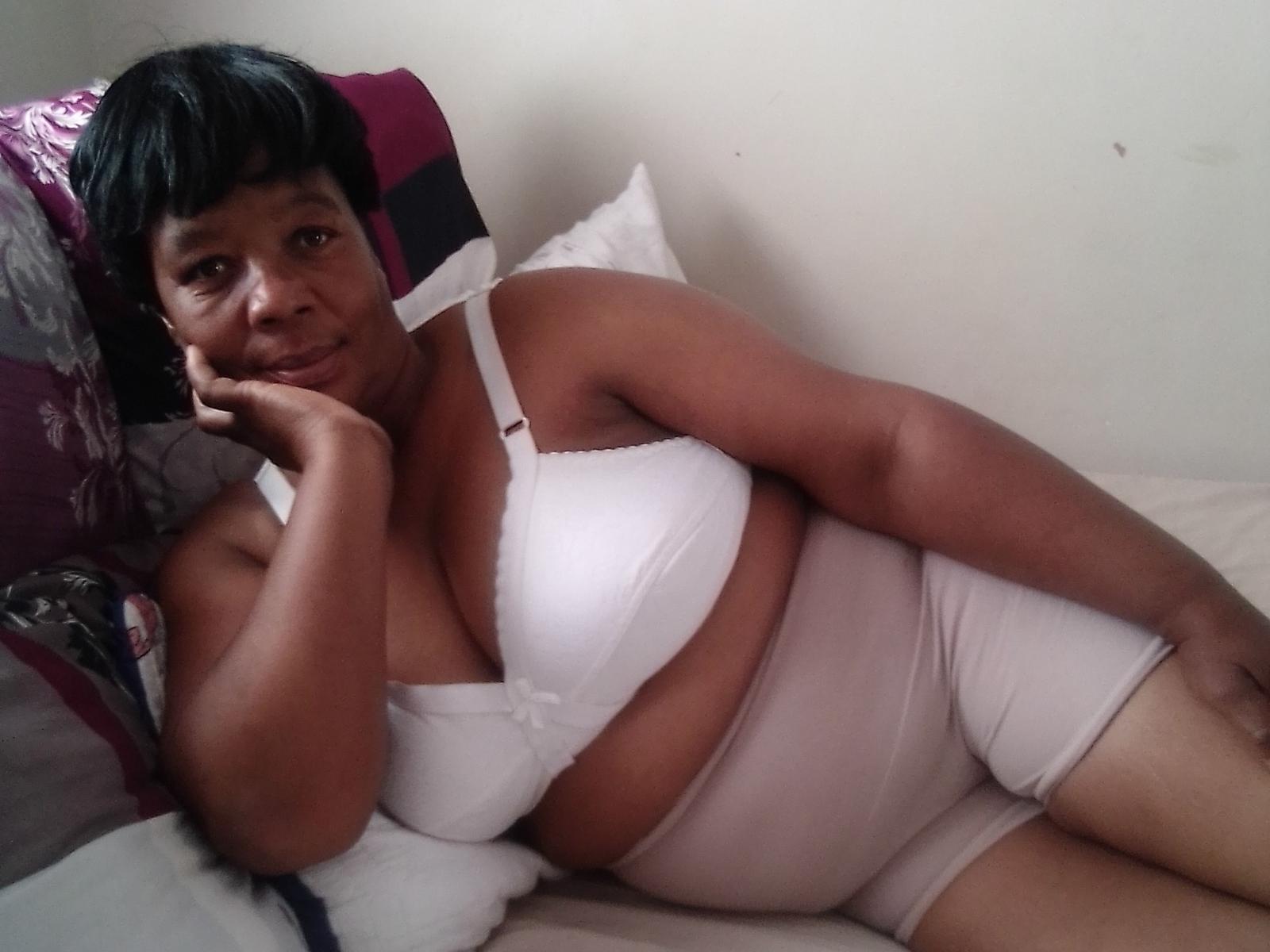 NomaHot with short black hair, medium brown skin, white bra, and white panties, lying on bed, resting head on hand, smiling, showing her tits and ass.