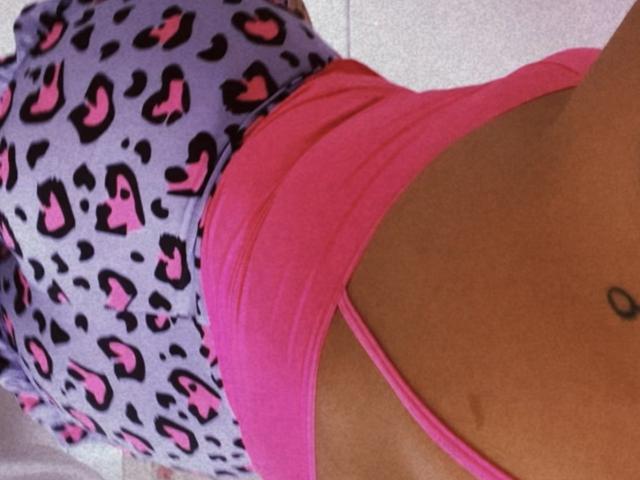 AnnneNaughtyBusty's pink sports bra and leopard print pants, showing her tan, flat stomach with a small black tattoo, and pink straps over her tits.