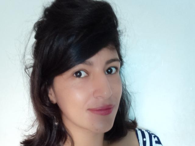 SarahFriendly with messy black hair, brown eyes, pink lips, light skin, wearing a blue and white striped shirt, looking at the camera with a slight smile.