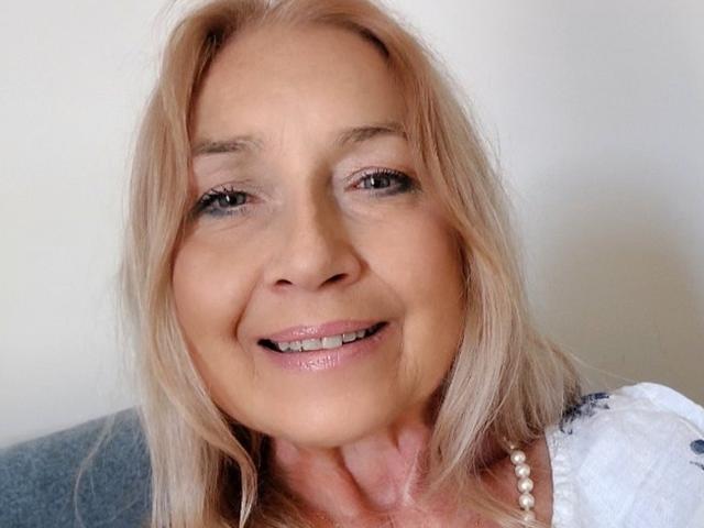 PerfectSofia's face, showing light blonde hair, subtle makeup, and a slight smile with shiny pink lips. She's wearing a white top with a pearl necklace.
