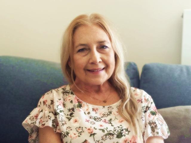 Blade-like letter "L" in the center, slightly blurred, with two small, detailed coins at the bottom. Coins have intricate designs, one with a crown. Warm, muted colors dominate.