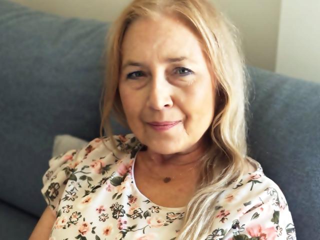 PerfectSofia has blonde hair, light skin, small nose, slight smile, and wears a floral shirt. She's sitting on a blue couch with a white pillow behind her.