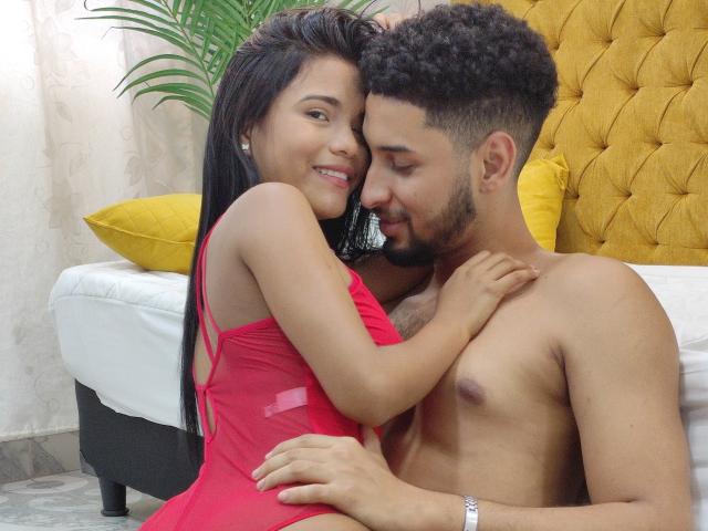 Karen e Alex, con lunghi capelli neri e un vestito rosso, abbracciano un uomo senza camicia, con i capelli ricci e la barba, entrambi sorridono, con le mani sul petto dell'altro, e sullo sfondo si vede una testiera gialla..
