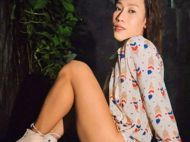 Darcy, zomerse hitte, met blote billen, knie omhoog, draagt een geruit shirt en witte sokken, donkere achtergrond, groene plant aan de linkerkant, bruin haar, subtiele glimlach, lichte huid, schattig gezicht..