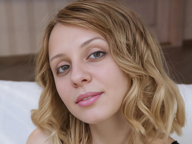 CleopatraVodos has blonde, wavy hair, light skin, green eyes, pink lipstick, and a subtle smile. Her cute face is centered, looking slightly to the left.