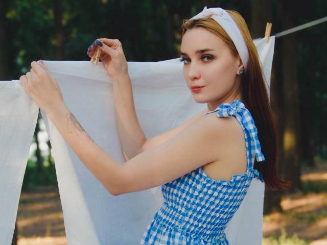 AlexisHott with blue checkered dress, white headband, holding white fabric, tattoo on forearm, smiling, looking back, forest background, sunlight, pink lips, cute, slim, fair skin, small tits.