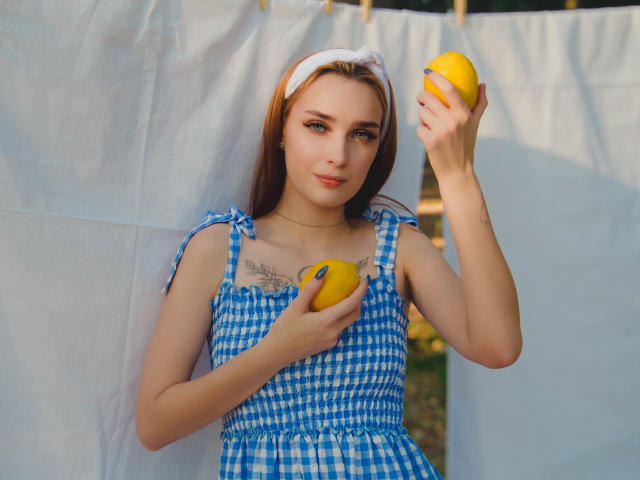 Alexishott with yellow lemons, wearing a blue and white checkered dress, white headband, holding one lemon in each hand, showing her tits and a tattoo under her chest.