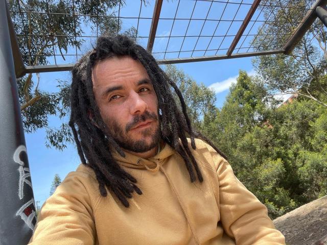 VictorPi ha dei dreadlocks neri di lunghezza media, una barba e indossa una felpa color sabbia. Il suo viso, con gli occhi azzurri e un'espressione leggermente compiaciuta, è in primo piano..