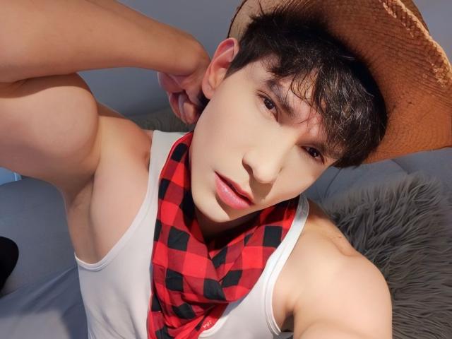 NeythanBlaze, muscular, wearing white tank top, red and black checkered scarf, brown hat, short dark hair, slightly parted lips, looking at camera, right arm raised.