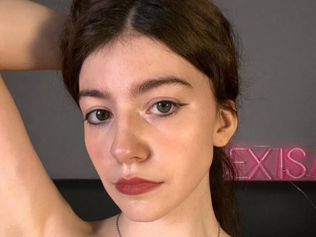 VinnaSkyHott has brown eyes, dark brown hair, and red lipstick. Her right arm is raised, showing her armpit. She's wearing a thin necklace. She looks directly at the camera.