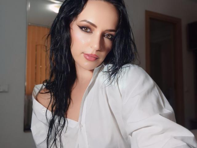 KairaFoxy69, con i capelli neri bagnati, indossa una camicia bianca con una spalla scoperta, ha labbra rosa carnose e occhi scuri e affumicati. Il suo seno è parzialmente visibile sotto la camicia..