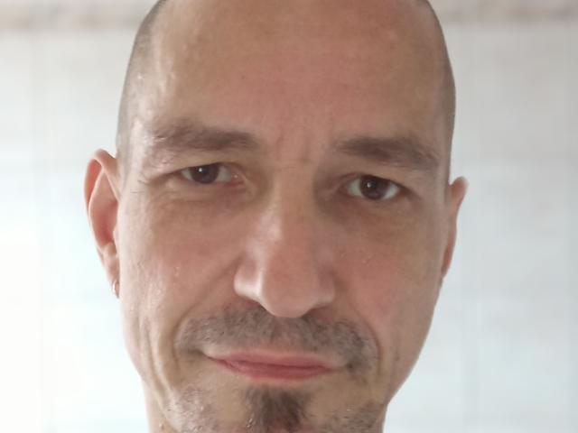 KlumsiMan heeft een kaal hoofd, lichte huid, bruine ogen, een dunne snor en een klein baardje. Zijn gezicht is lichtelijk gerimpeld met een subtiele, gesloten glimlach..