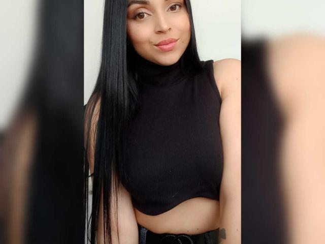 HikariChloe has long black hair, a cute smile, and is wearing a black sleeveless crop top that shows her midriff. Her small tits are slightly visible under the top.