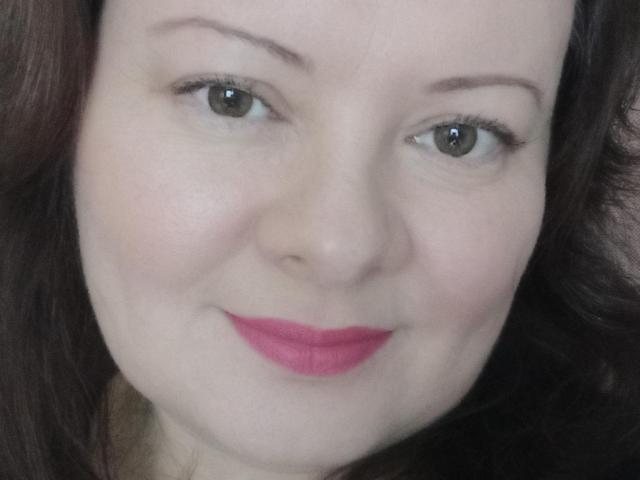 MayDreamy's face with fair skin, brown eyes, and pink lipstick, smiling slightly. She has dark brown, wavy hair and light brown eyebrows. Her tits aren't visible.