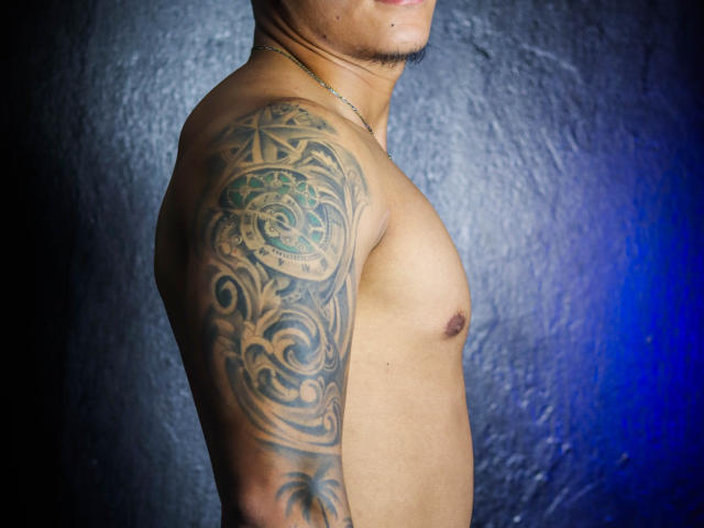 Shirtless JeisonStark with a detailed, ornate tattoo covering his right shoulder and upper arm, dark skin, short goatee, necklace, and a small nipple. Blue light on the right.
