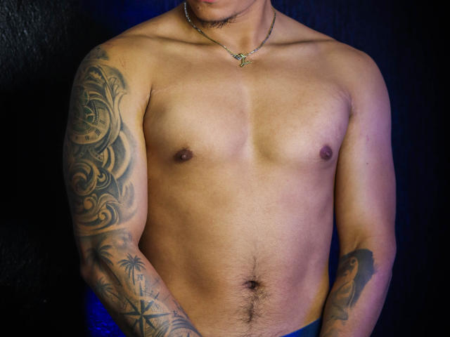 JeisonStark's shirtless upper body, with tattoos on both arms, a necklace, and a slight tan. His small, dark nipples and a small patch of pubic hair are visible.