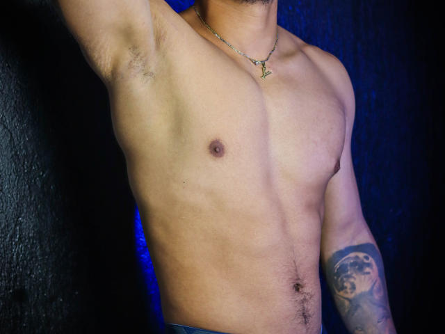 JeisonStark's shirtless upper body with a tattooed arm, small nipples, and a necklace. His tan skin and blue jeans are visible, showing a muscular chest and slight chest hair.