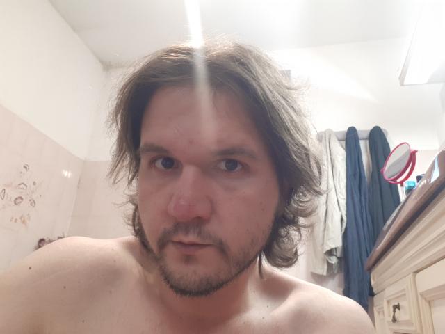 NectarineFad has messy brown hair, a small goatee, and a slightly puffy face with a small boogers. He's shirtless with a neutral expression.
