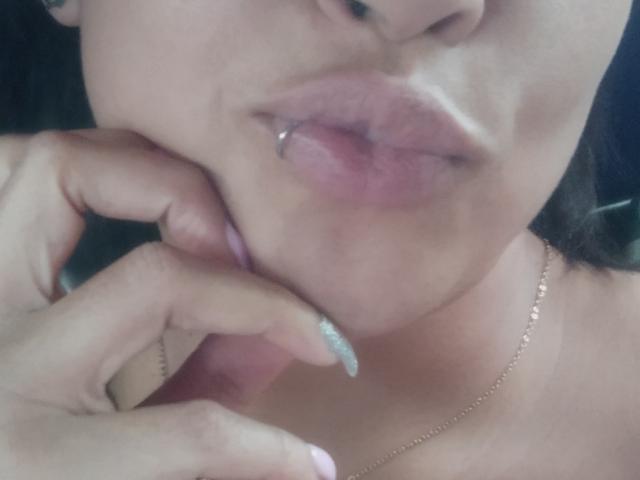 MirandaDreams' puffy pink lips with a silver lip ring, slightly parted, touching her lower lip with a glittery nail. She's wearing a gold necklace.