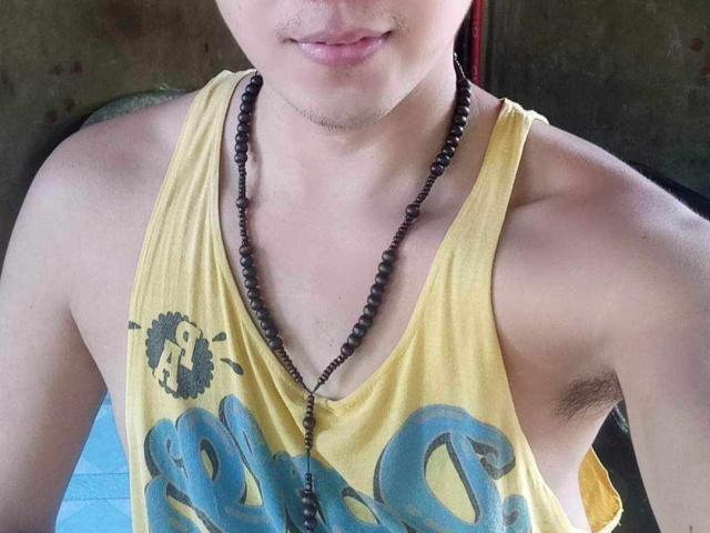 Saphira69's yellow tank top, showing armpit hair, with a black bead necklace, and a partial smile, head slightly out of frame, light skin, subtle stubble.