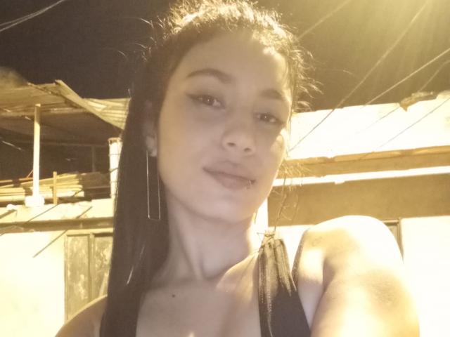 KataleyaMansson has light skin, black straight hair, and is wearing a black tank top. She's showing a slight smile with her lips slightly parted. Her tits are visible.