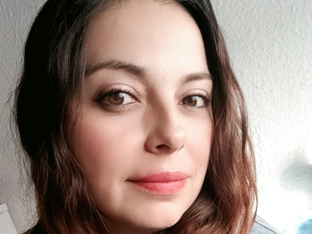 Seher has a cute face with brown eyes, slightly wavy dark brown hair, and pink lips. Her skin is fair and she's smiling subtly.